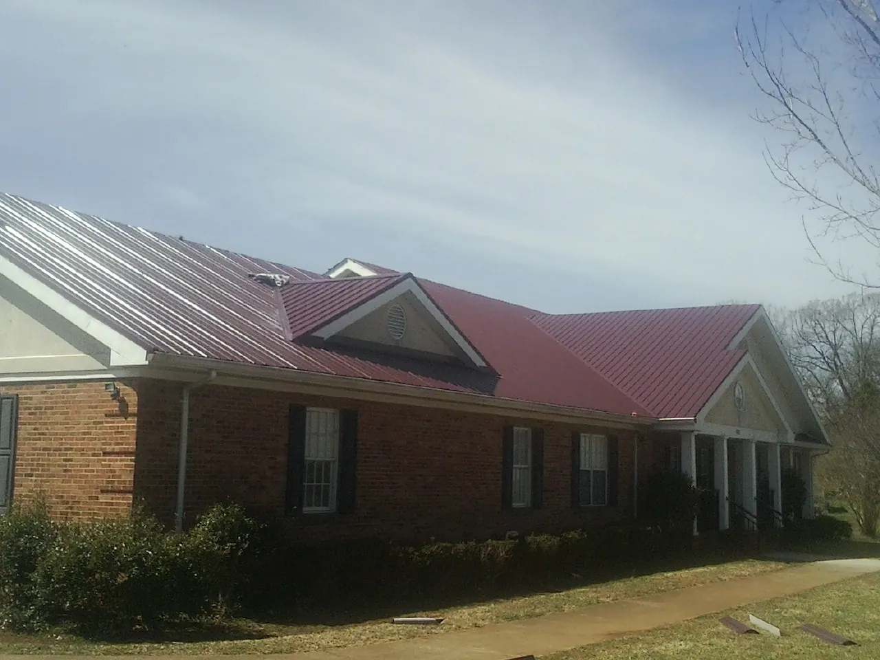 Red metal roof with gabled entries on a long brick building, from a Hail Damage Roof Repair job in Mound City