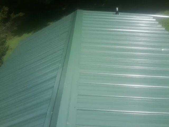 New green metal panels meeting at the ridge of a roof — Flat Roof Repair work by our crew in Mound City