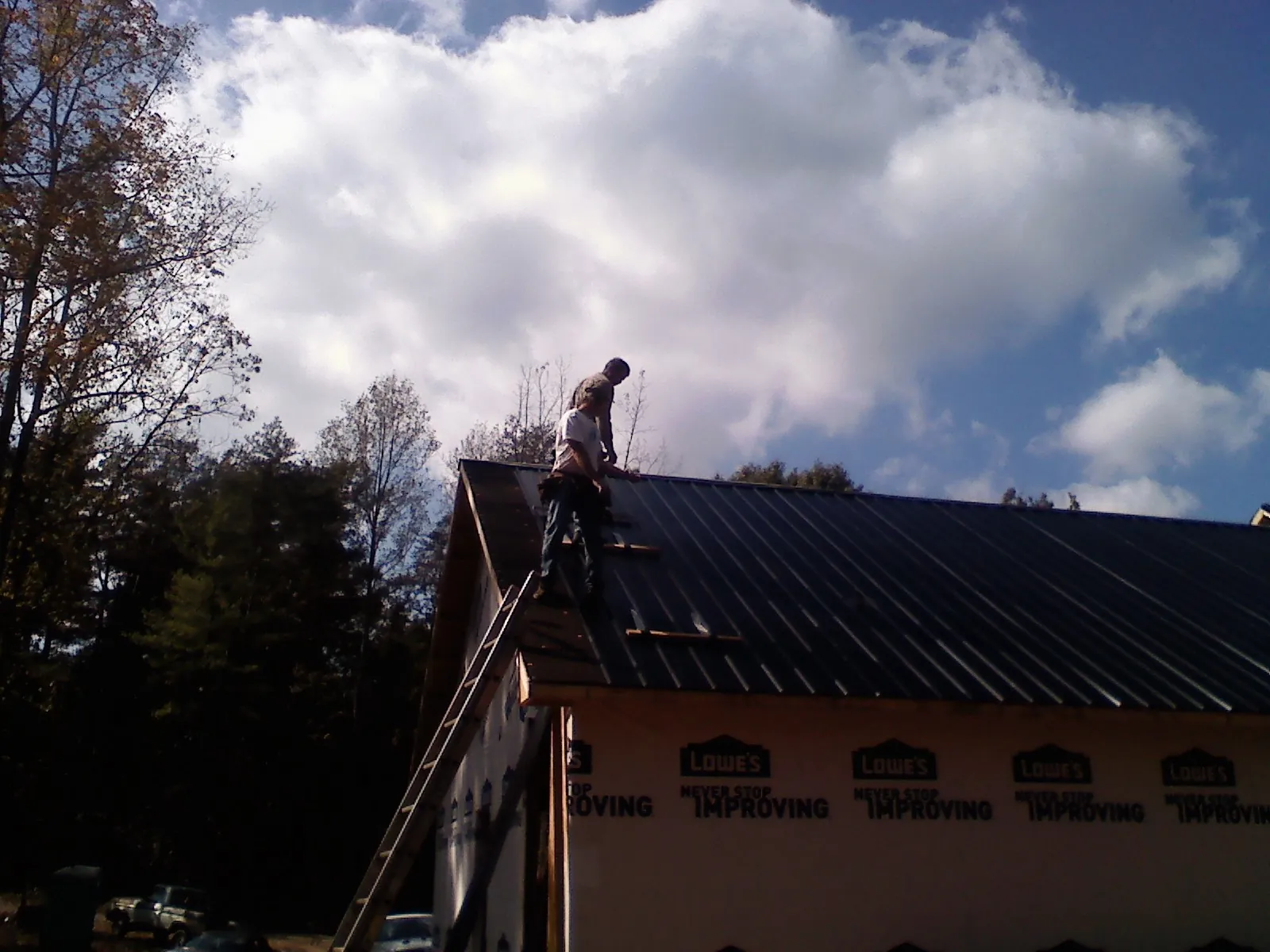 Roofer fastening dark metal panels high against a cloudy sky, from a Roof Inspection job in Mound City
