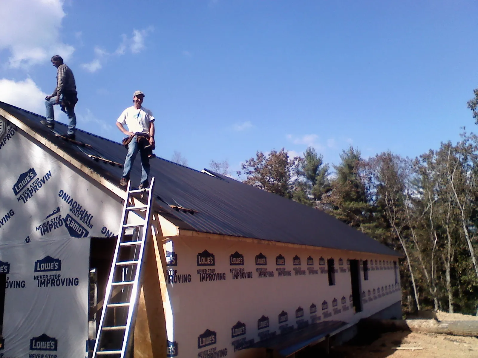 Two roofers standing on a long dark metal roof over a wrapped building in Mound City