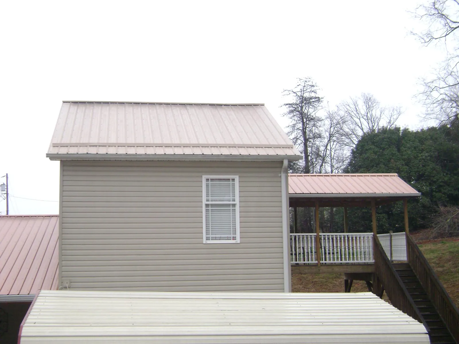 Tan metal roofs on a two story addition and attached porch, from a Roof Replacement job in Mound City